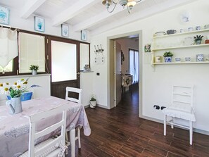 A room with a dining table, chairs, a window with blinds, a hallway, and a shelf with decorative items. - La Casa di Menny by Interhome (Moneglia)