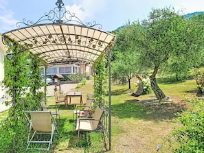 A covered outdoor seating area with chairs and a table, surrounded by greenery and a view of a building in the background. - La Casa di Menny by Interhome (Moneglia)