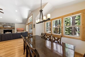 A dining area with a large wooden table, multiple chairs, and a stone fireplace. - Family Delight at Tahoe (South Lake Tahoe)