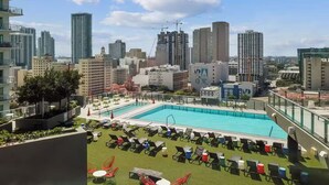 Una piscina sul tetto con sedie a sdraio, vista sullo skyline della città e un edificio con il logo ben visibile.