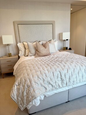 A neatly made bed with a patterned bedspread and multiple pillows, a bedside table with a lamp, and a nightstand with drawers. - Cosy 1 bedroom luxe apartment in the heart of London (London)