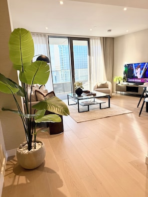 A modern living room with a large flat-screen TV, comfortable seating, and a large window with a city view. - Cosy 1 bedroom luxe apartment in the heart of London (London)