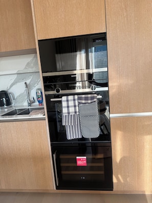 Een keuken met een inbouwoven, een magnetron, een roestvrijstalen spoelbak en een koffiezetapparaat.