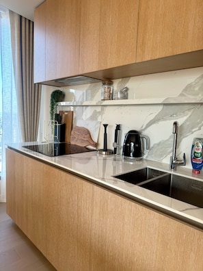 A modern kitchen with a marble countertop, stainless steel sink, and wooden cabinets. - Cosy 1 bedroom luxe apartment in the heart of London (London)