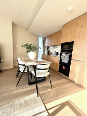 A modern kitchen with wooden cabinets, a built-in oven, and a dining area with a marble table and fluffy chairs. - Cosy 1 bedroom luxe apartment in the heart of London (London)