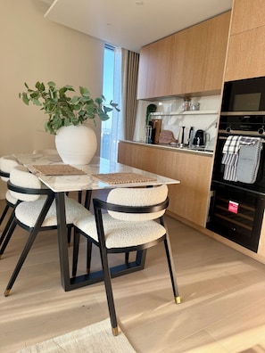 A modern kitchen with a built-in oven, a dining area with a marble table and cushioned chairs, and a large potted plant. - Cosy 1 bedroom luxe apartment in the heart of London (London)