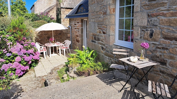 A stone building with a window, a table with chairs, and a small garden with pink flowers. - Coastal Stone House in Lannilis for 5 (Lannilis)