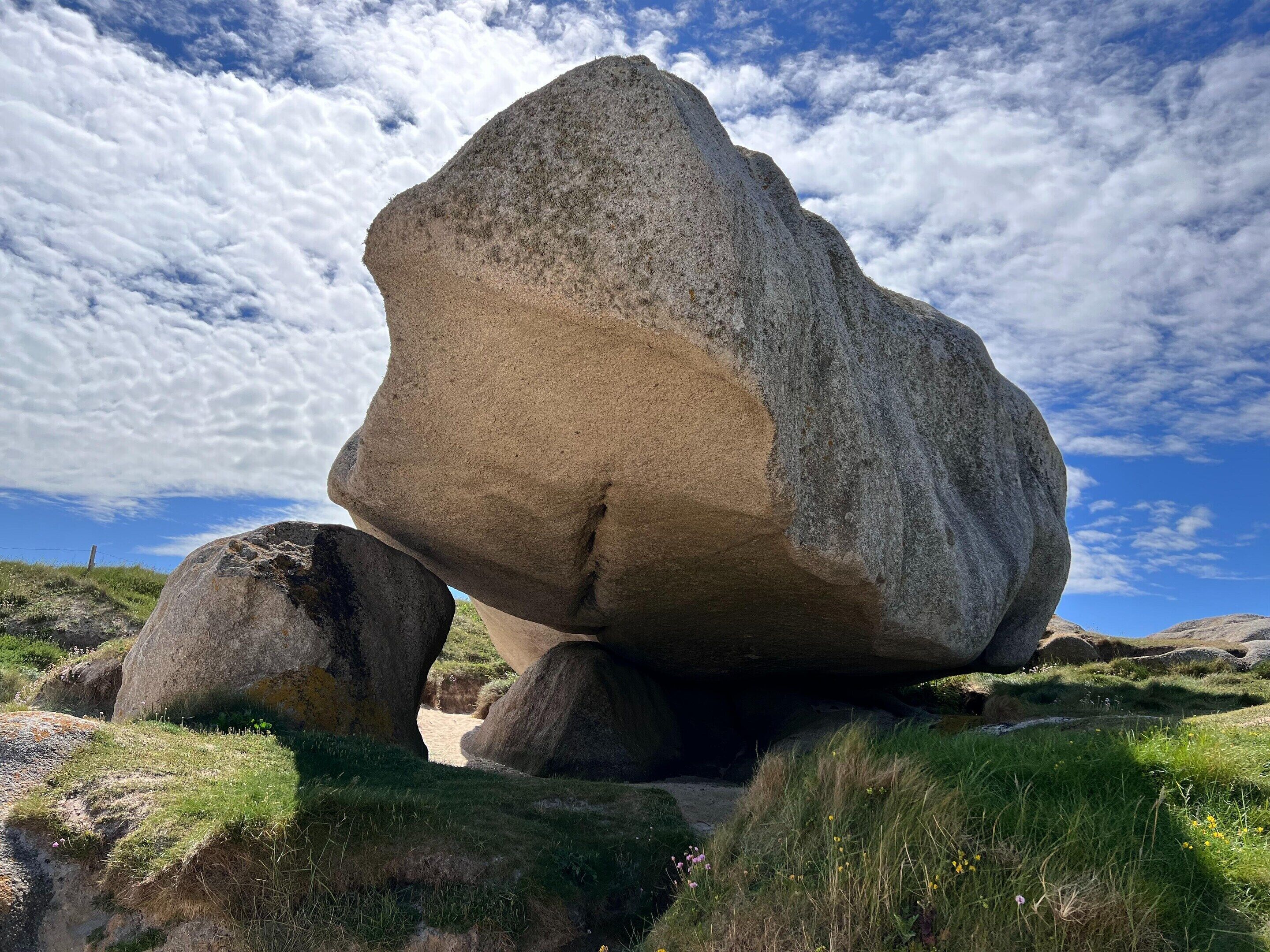 Ein großer Felsbrocken, der auf kleineren Felsen in einem grasbewachsen Feld unter blauem Himmel balanciert.