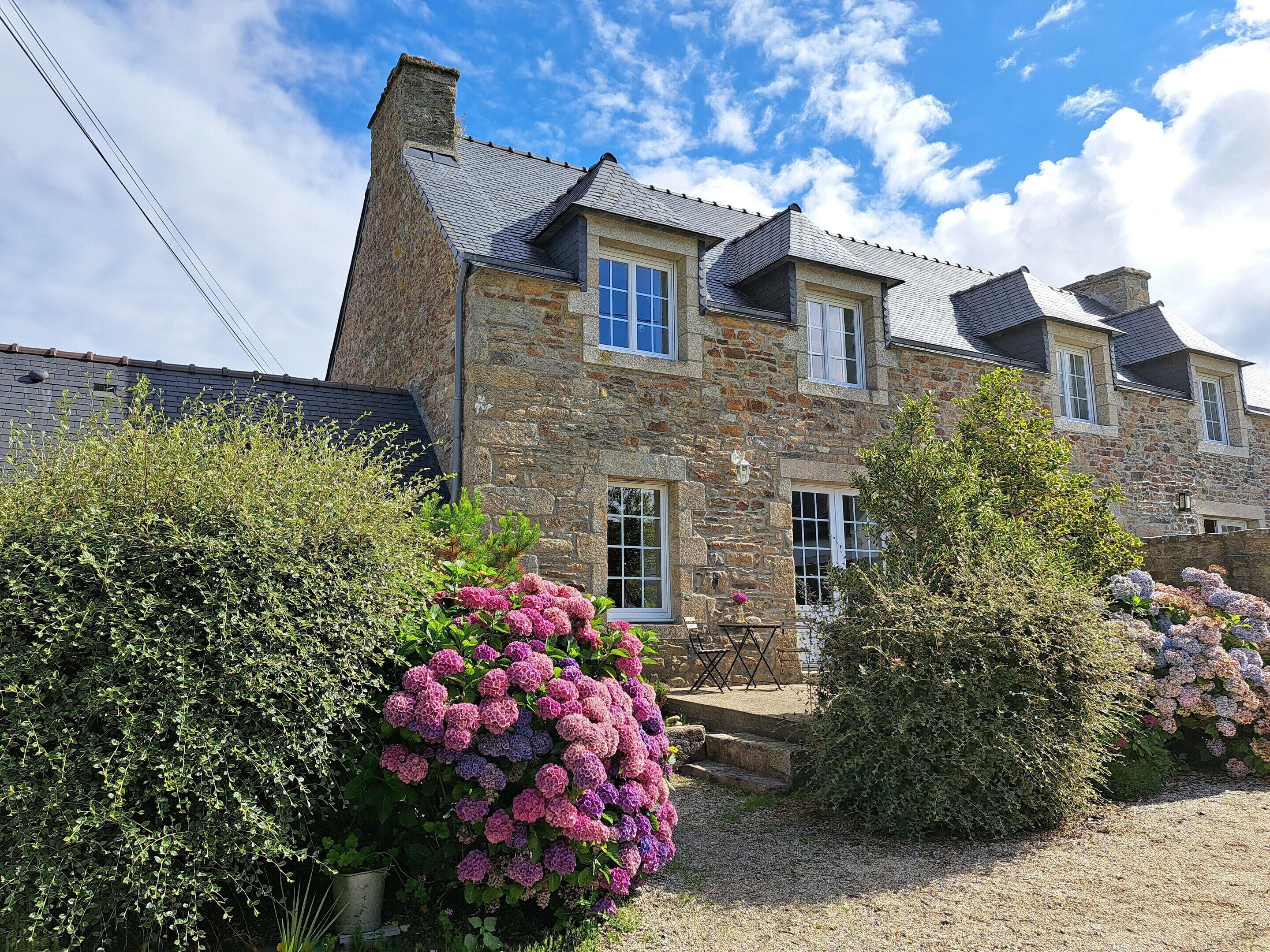 Une maison en pierre avec une allée en gravier et une végétation luxuriante.