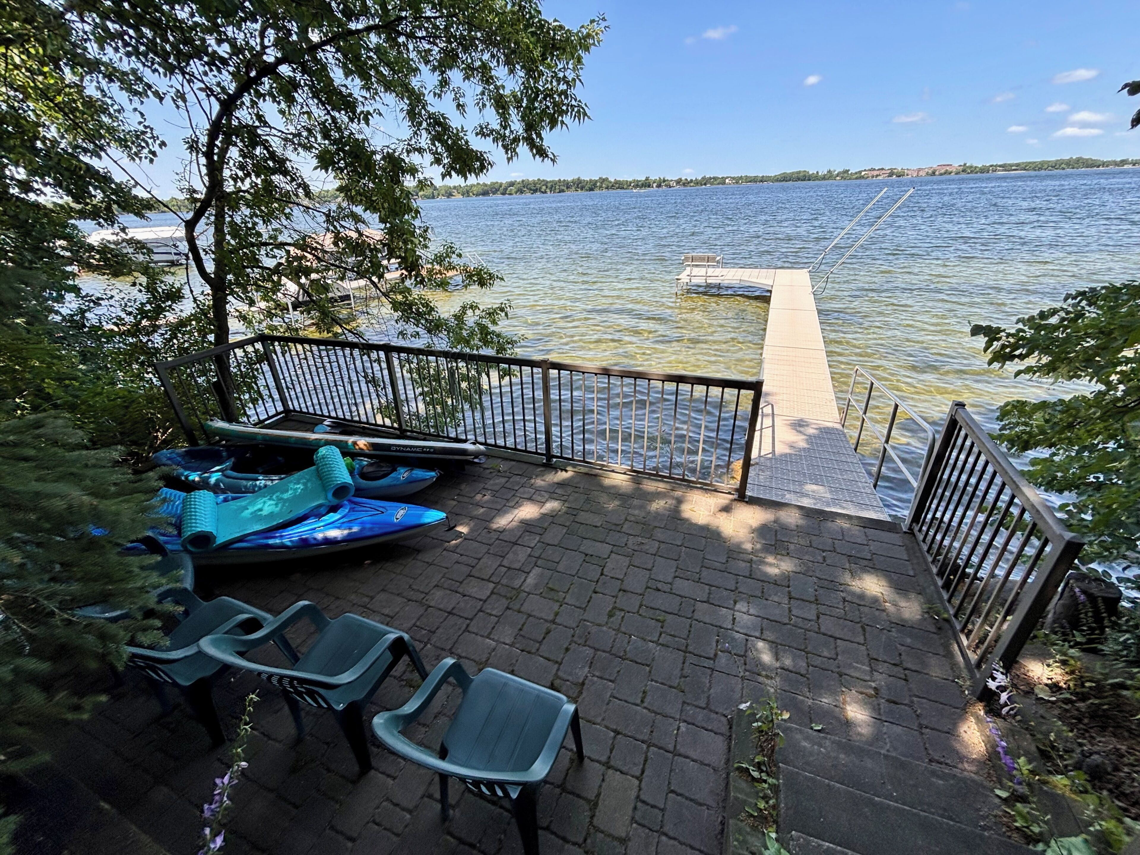 A dock with kayaks and chairs, a clear view of the lake, and a distant shoreline.