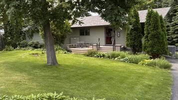 Une maison avec un jardin devant, une petite terrasse et un arbre.