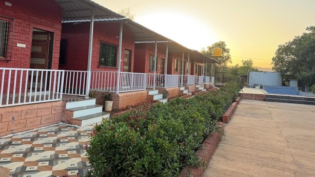 A row of red brick buildings with white railings, a tiled walkway, and a clear sky. - Ivystone Cottages (Bhilar)