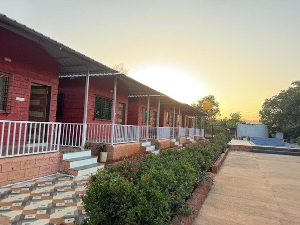 A row of red brick buildings with white railings, a tiled walkway, and a clear sky. - Ivystone Cottages (Bhilar)