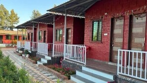 A row of red brick buildings with white railings and a patterned tile walkway. - Ivystone Cottages (Bhilar)