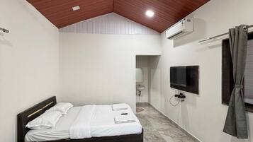 A bedroom with a bed, a ceiling fan, an air conditioning unit, a television, and a bathroom visible in the background.