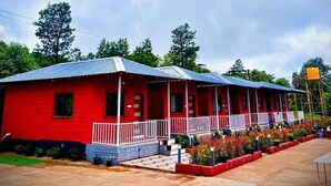 A red building with a blue roof, a covered porch, and a paved area with potted plants. - Ivystone Cottages (Bhilar)