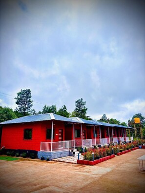 Un edificio rojo con techo azul, un porche cubierto y un patio empedrado con plantas en macetas.