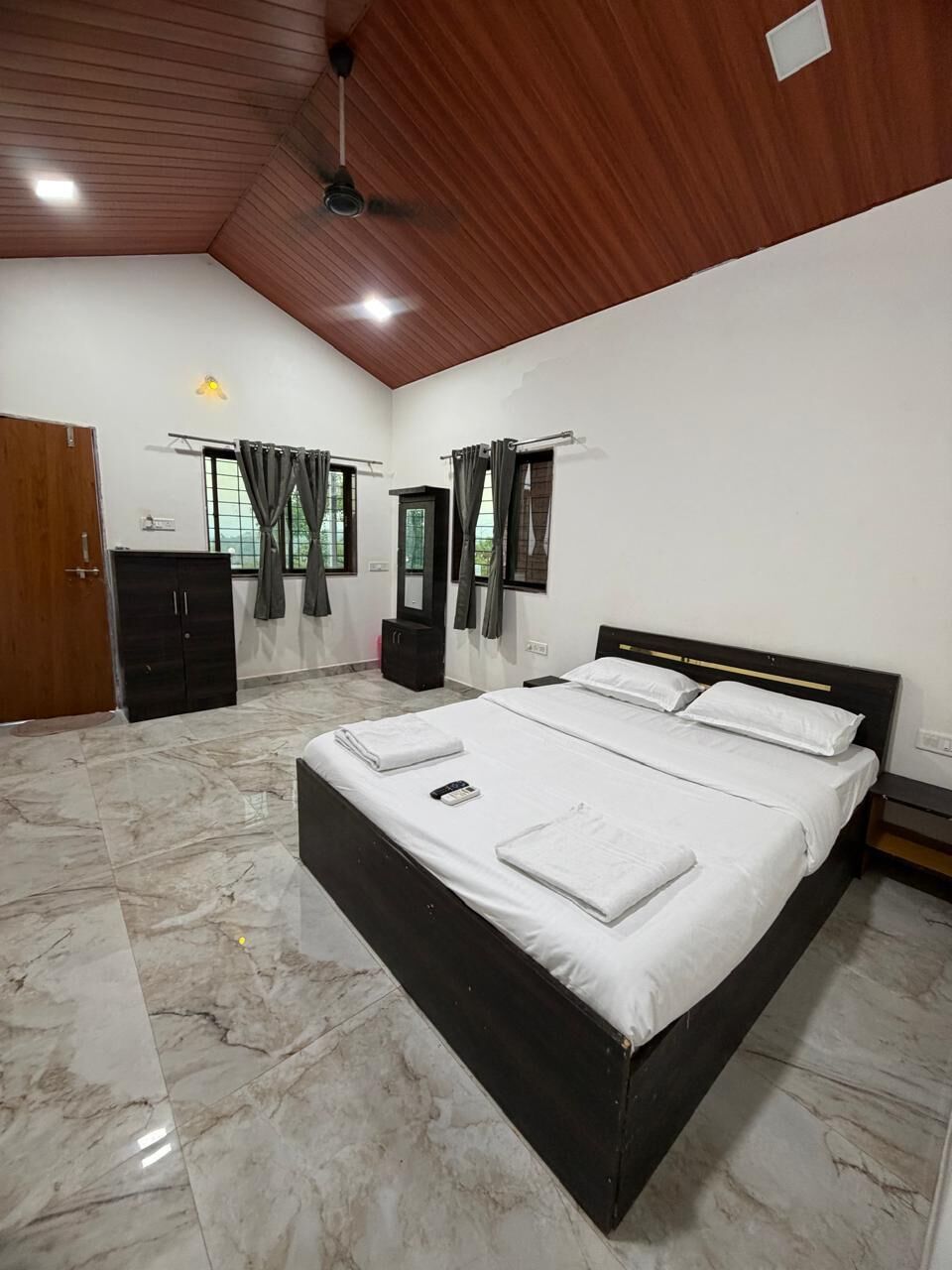 Une chambre à coucher avec un lit, une armoire, un ventilateur de plafond et une fenêtre avec des rideaux.