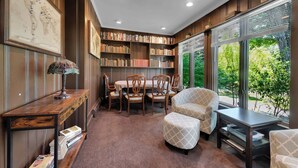 Una stanza con una libreria in legno, un tavolo da pranzo con sedie, un globo su un tavolo consolle e un'ampia finestra vista sul verde.
