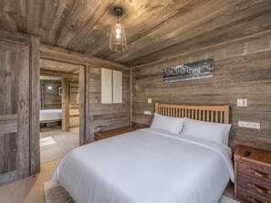 A wooden room with a bed, a wooden headboard, a nightstand, a suitcase, and a wall-mounted light fixture. - Modern apartment, south terrace - 4 guests (Méribel Village)