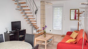 Un salon moderne avec un escalier en colimaçon, un téléviseur, un canapé rouge et une table basse.