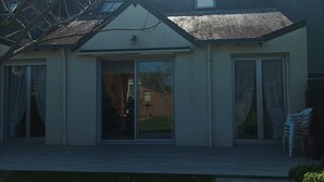 Yhden kerroksen talo, jossa on etuovi, liukuvat lasiovet ja pieni kuisti.