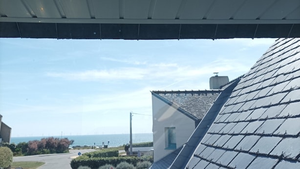 A residential building with a sloped roof, a clear view of the sea, and a street with parked cars. - House, pets allowed - 6 guests, 100m from the sea (Le Croisic)