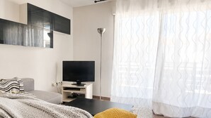Een moderne kamer met een flatscreen televisie op een standaard, een bank met een plaid, een geel kussen en een vloerlamp.