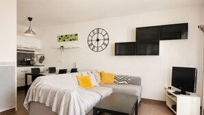 Een moderne woonkamer met een bed, een bank, een televisie en een keukenhoek.