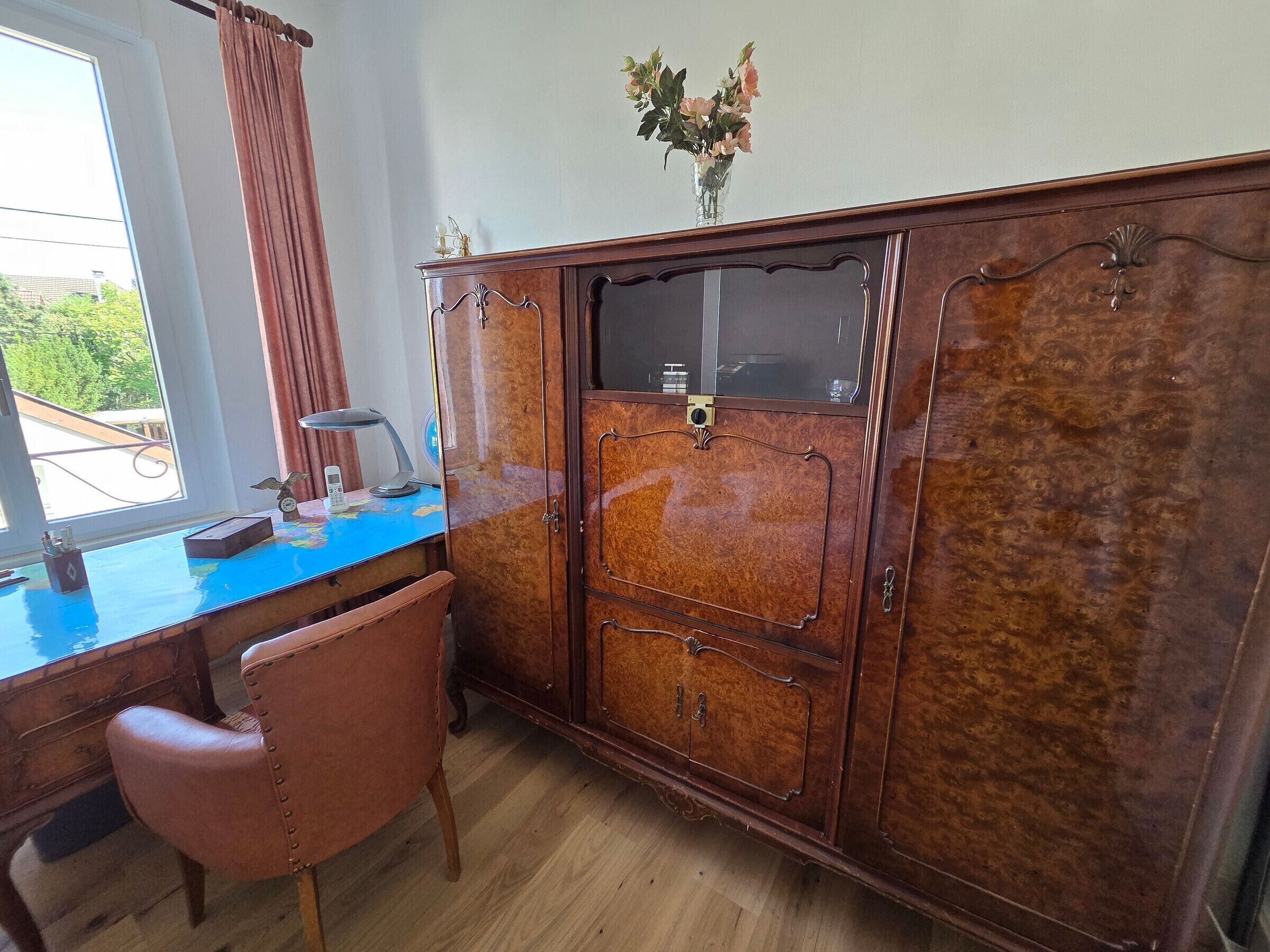A room with a wooden desk, a chair, a cabinet with glass doors, and a window with curtains.