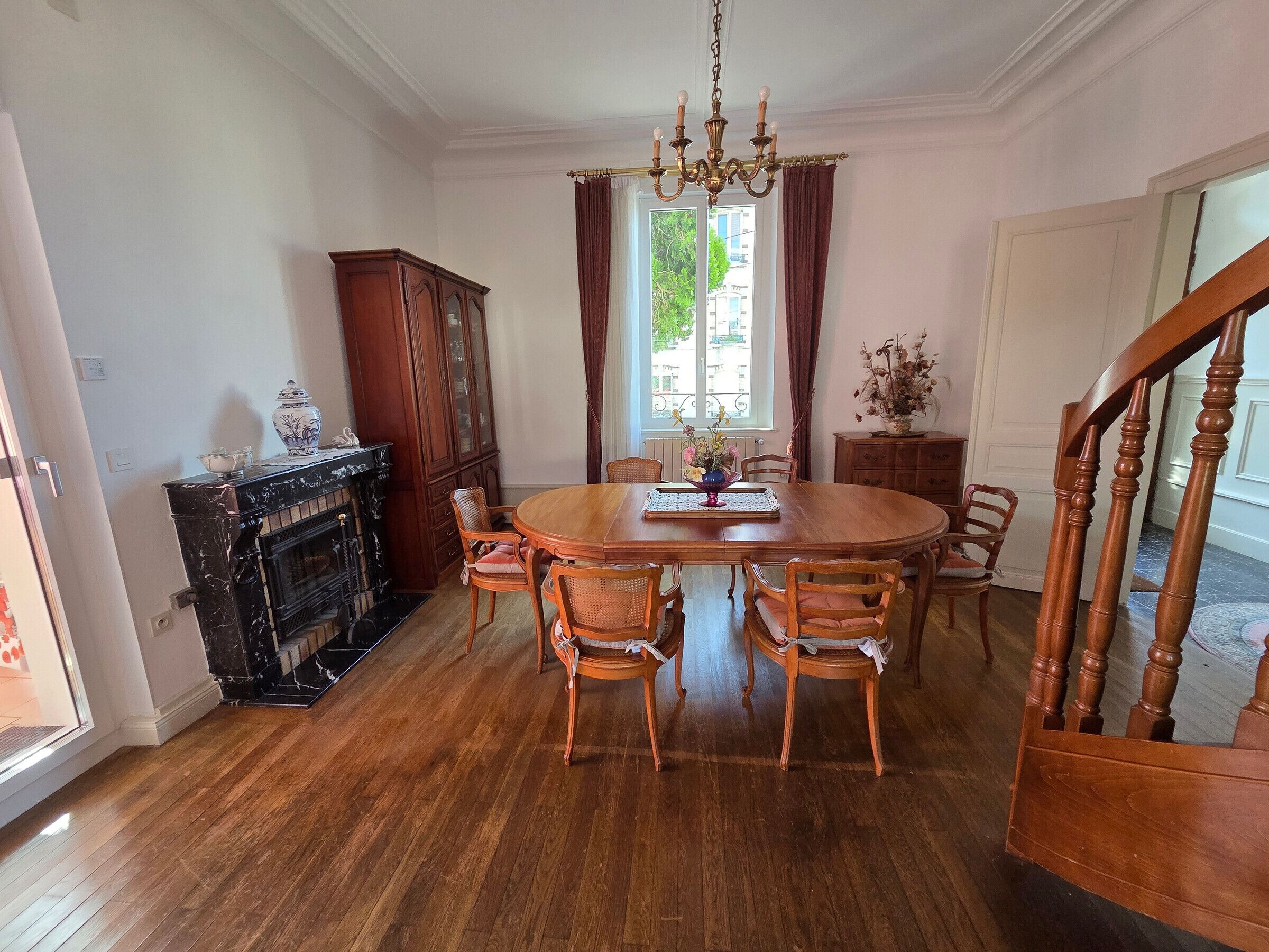 Un comedor con una mesa de madera, sillas, una araña y una chimenea.