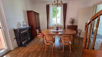 Un comedor con una mesa de madera, sillas, una araña y una chimenea.