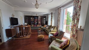 Una sala de estar con piso de madera, televisor, estantería y balcón con cortinas.