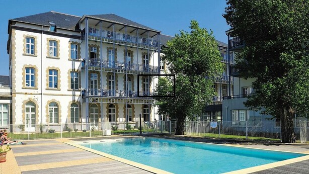 Un edificio a più piani con piscina, terrazza in legno e area recintata.