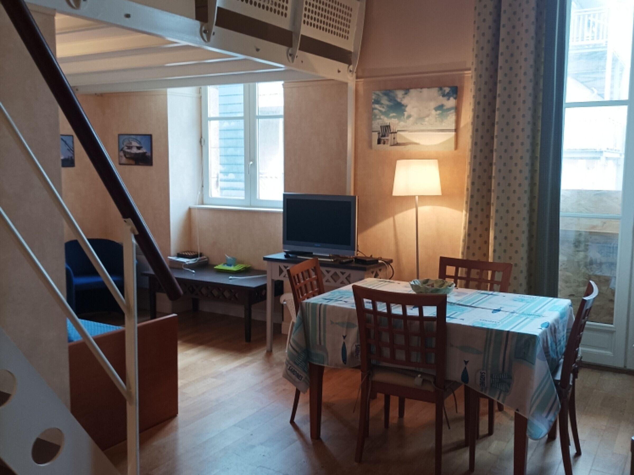 Huone, jossa on ruokapöytä, tuoleja, televisio, lamppu ja portaikko.