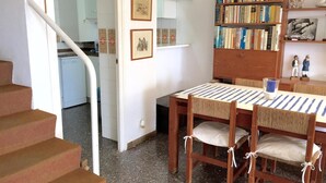 Zona pranzo con tavolo e sedie in legno, una libreria e una scala.
