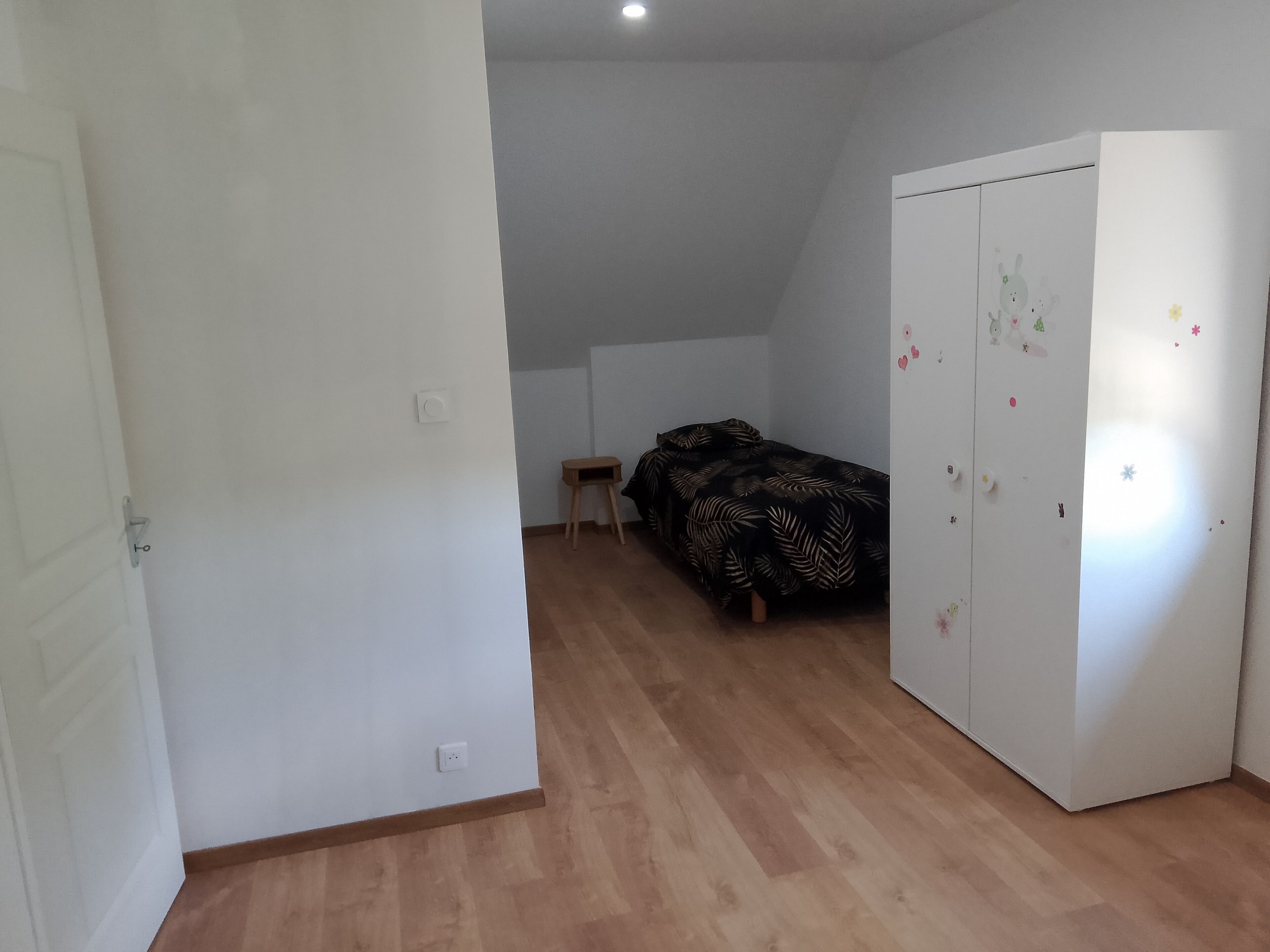 Un dormitorio con cama, armario, mesita y puerta.