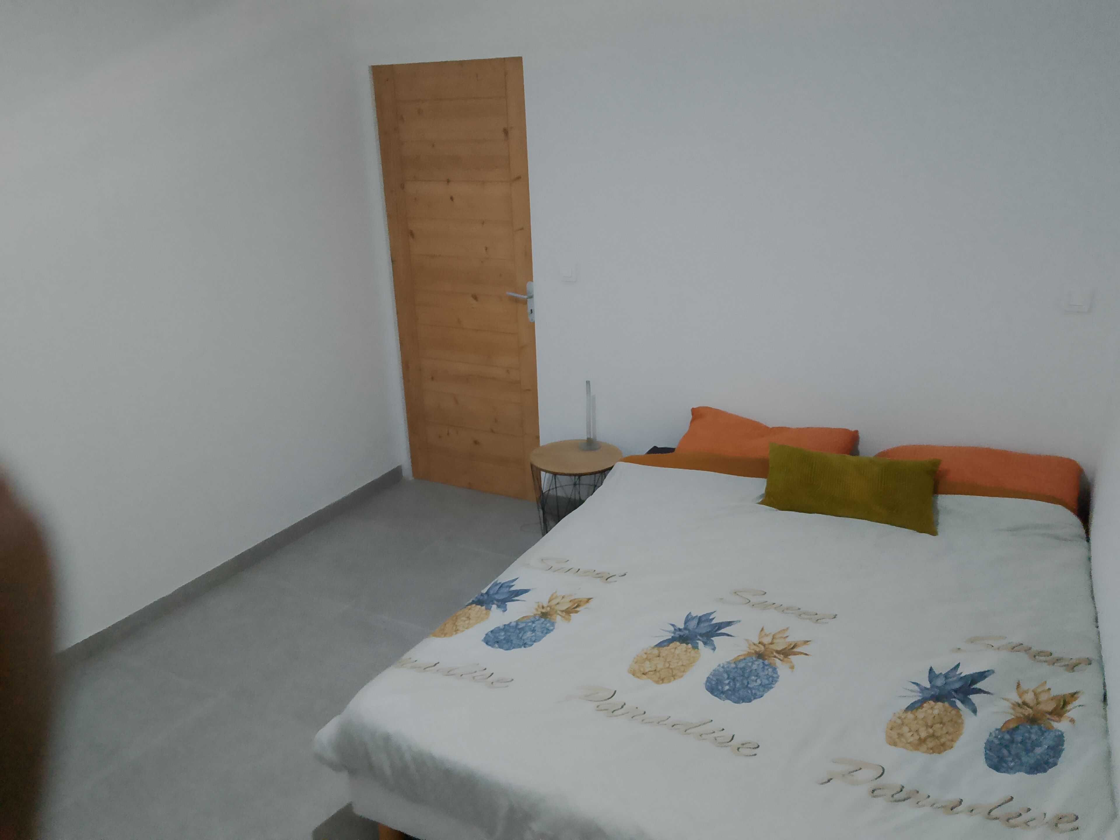 A bedroom with a bed, pillows, a wooden door, and a small round table.