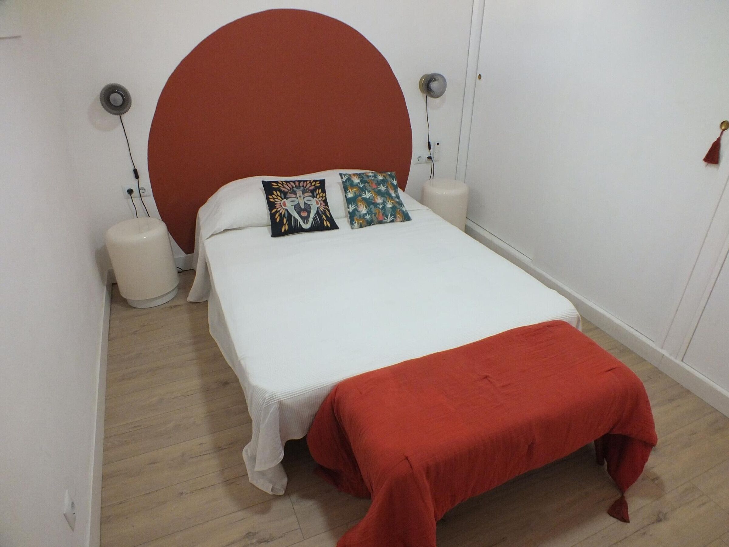 Una cama con cabecera roja, ropa de cama blanca y dos almohadas con diseños diferentes.