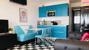 Um espaço compacto com cozinha compacta, área de refeições com mesa e cadeiras pequenas, sofá e televisão.