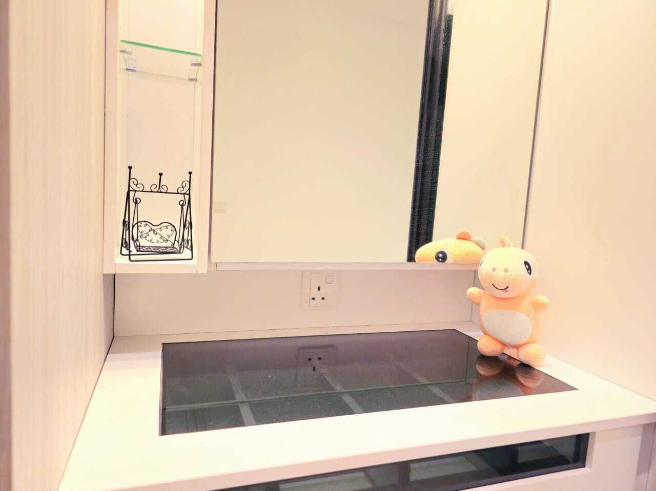 Un baño con espejo, lavamanos y un peluche en la encimera.
