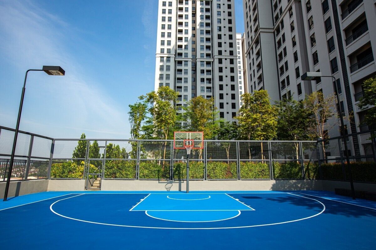An outdoor basketball court with a net, surrounded by a fence, and tall buildings in the background.