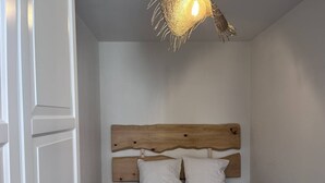 A bedroom with a wooden headboard, white bedding, a blue throw blanket, and a unique hanging light fixture. - Quiet apartment with parking - 4 guests (Cauterets)