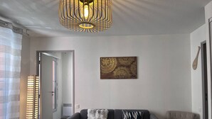 A modern living room with a sofa, a chair, a floor lamp, a pendant light, and a decorative wall piece. - Quiet apartment with parking - 4 guests (Cauterets)