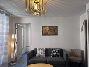 Ein stilvolles Wohnzimmer mit einer Couch, einem Sessel, einer Stehlampe, einer Pendelleuchte und einem Wandkunstwerk.