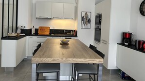 A modern kitchen with white cabinets, a wooden dining table, black chairs, a coffee maker, and a clock on the wall. - Modern apartment with parking - 4 guests (Le Lavandou)