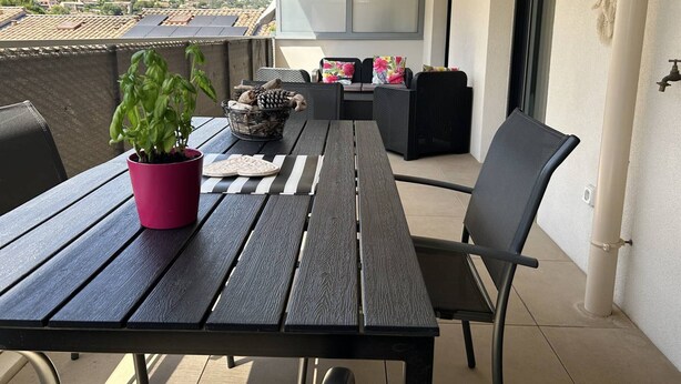 A balcony with a table, chairs, a potted plant, and a view of a village. - Modern apartment with parking - 4 guests (Le Lavandou)