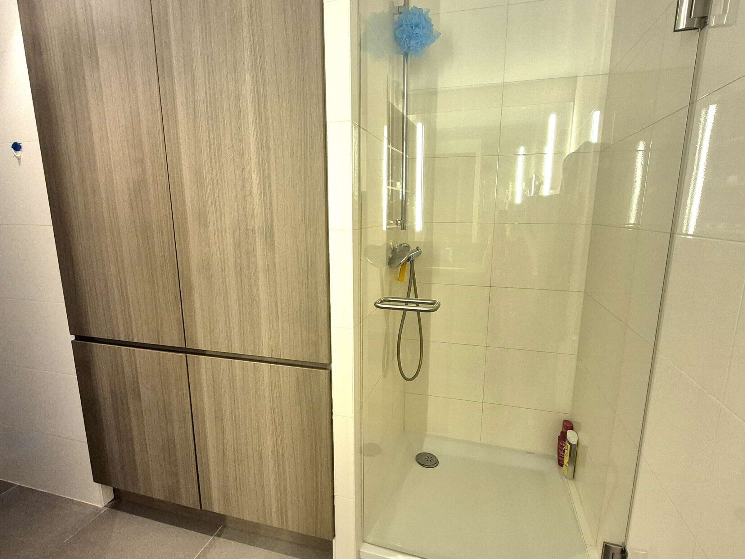 Une salle de bain avec une douche à parois de verre, un meuble en bois et un sol carrelé.