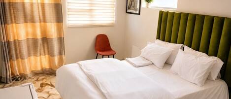 A hotel room with a bed, a chair, a window, and a curtain.
