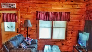 A cabin interior with a leather couch, a wooden rocking chair, a television on a stand, and a lamp. - Tennessee Dreams  Close to it all! (Pigeon Forge)